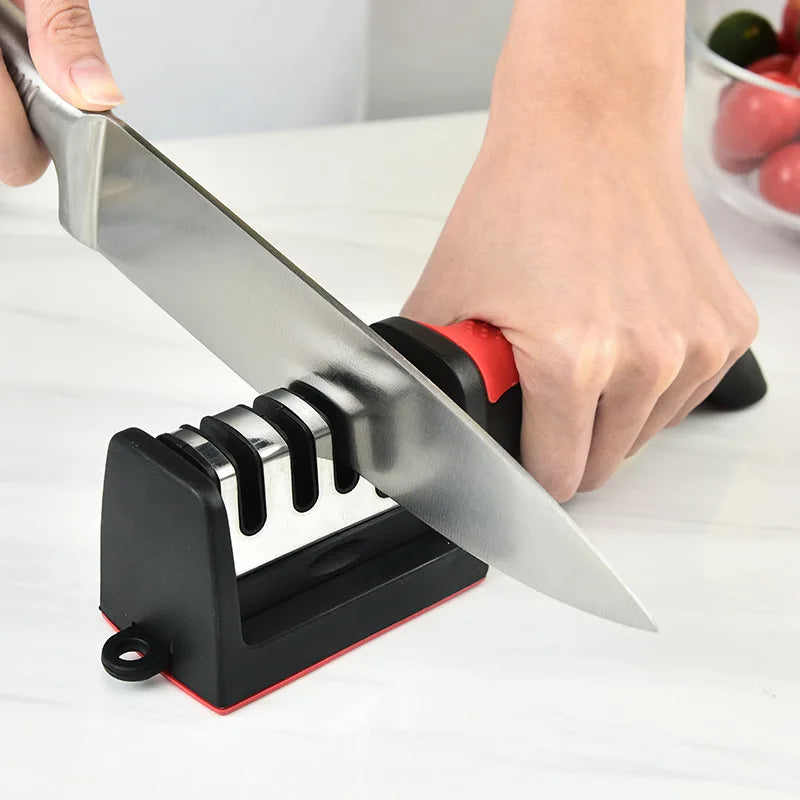 A hand is using a black and red handheld knife sharpener to sharpen a stainless steel knife blade.