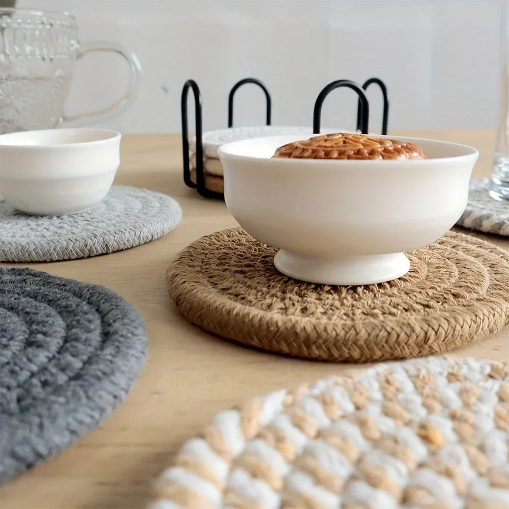 A set of four woven absorbent coasters in various shades of gray and natural fiber textures arranged on a wooden table.