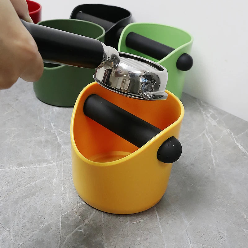 A yellow coffee grounds container with a black plunger is shown next to other green containers.