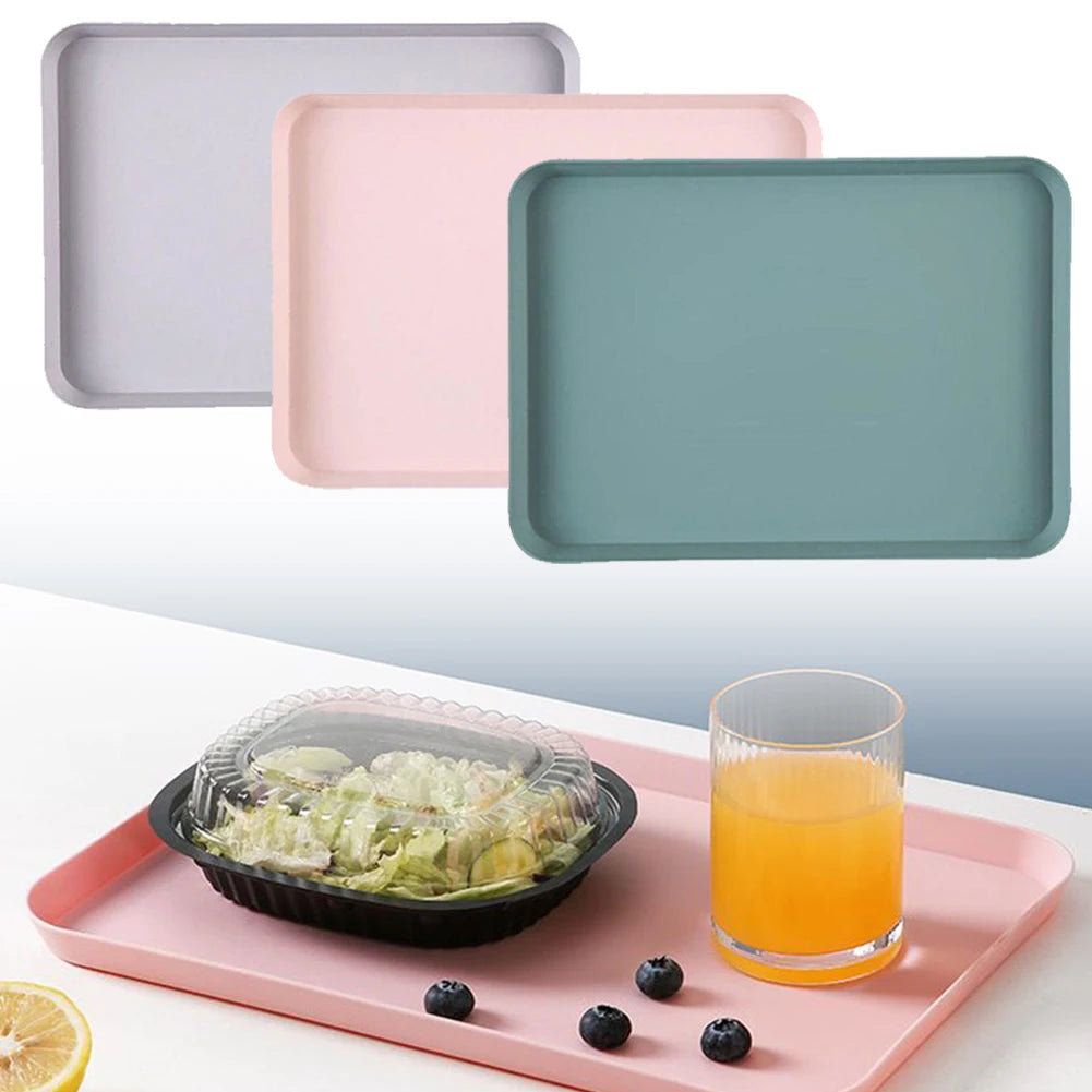 Three rectangular serving trays in light gray, pink, and teal are displayed on a pink tray with a glass of juice.