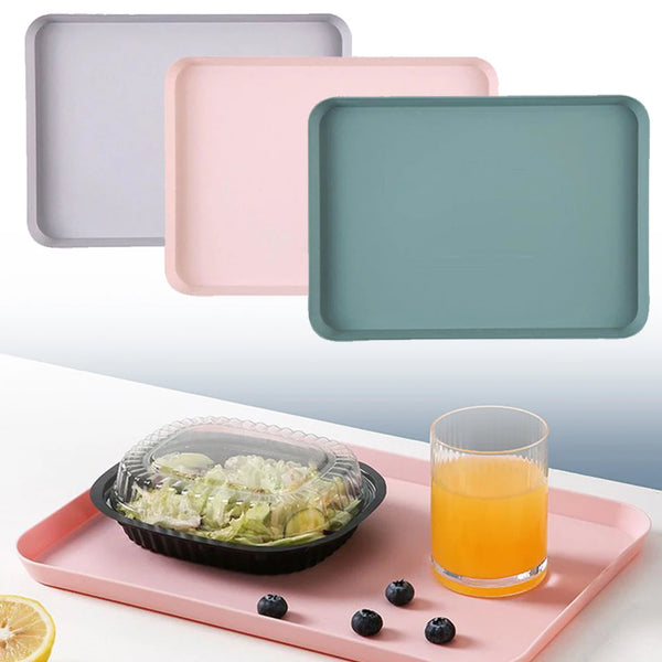 Drei rechteckige Servierteller in hellgrau, rosa und türkis auf einem rosa Tablett mit einem Glas Saft.