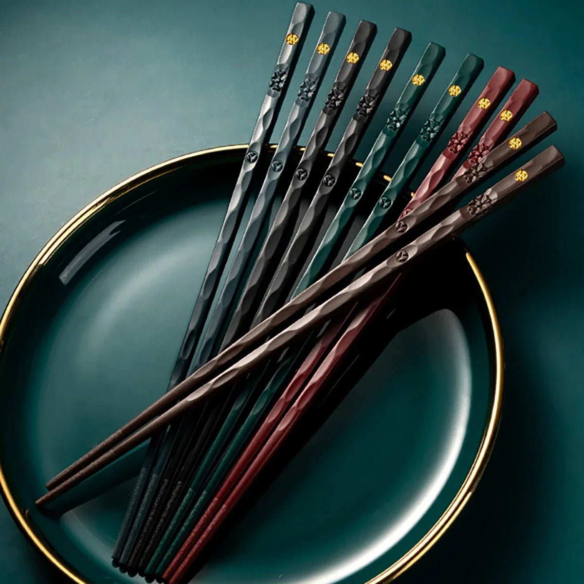 A set of five pairs of reusable food-grade metal chopsticks in various dark colors resting on a green plate.