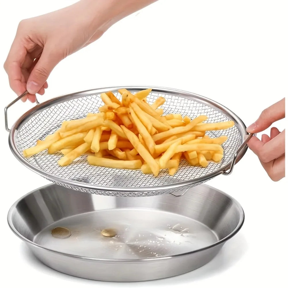 A hand is lifting a metal frying rack filled with golden french fries over a stainless steel bowl.