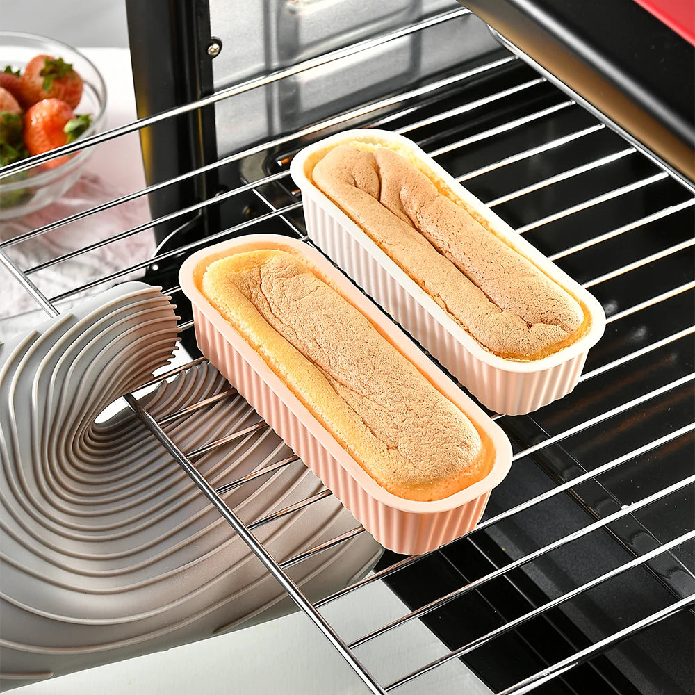 A set of silicone mini loaf baking pans filled with light brown baked goods resting on a metal rack in an oven.