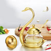 A gold-colored elegant condiment storage jar set featuring a curved spoon and a lid, displayed on a wooden board with chili p