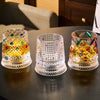 Three rotating whiskey glasses with colorful facets are displayed on a dark surface.