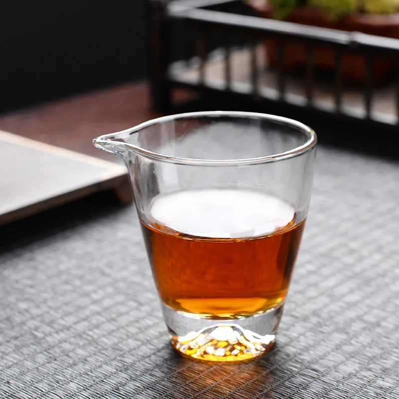 A clear glass teapot filled with amber tea is displayed on a dark surface.