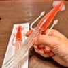 A hand holds a red squid cuttlefish themed fork and a small piece of the same product on a white plate.