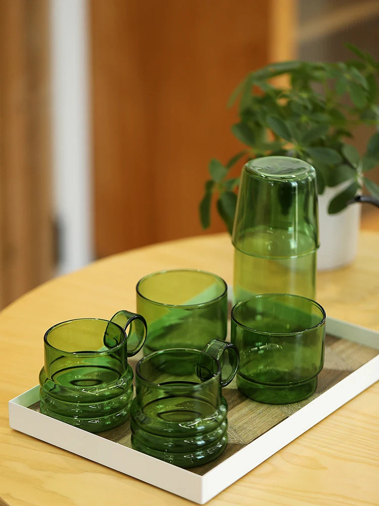 A set of elegant green glass teacups and mugs displayed on a wooden tray.