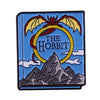 A blue enamel pin featuring a silhouette of a wizard bat and a mountain design with the text The Hobbit.