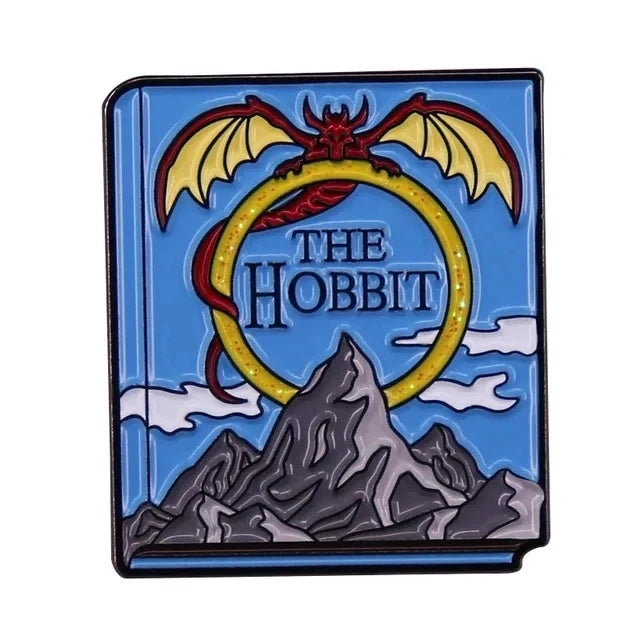 A blue enamel pin featuring a silhouette of a wizard bat and a mountain design with the text The Hobbit.