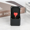 A black box containing a red heart-shaped item with a coiled wire inside