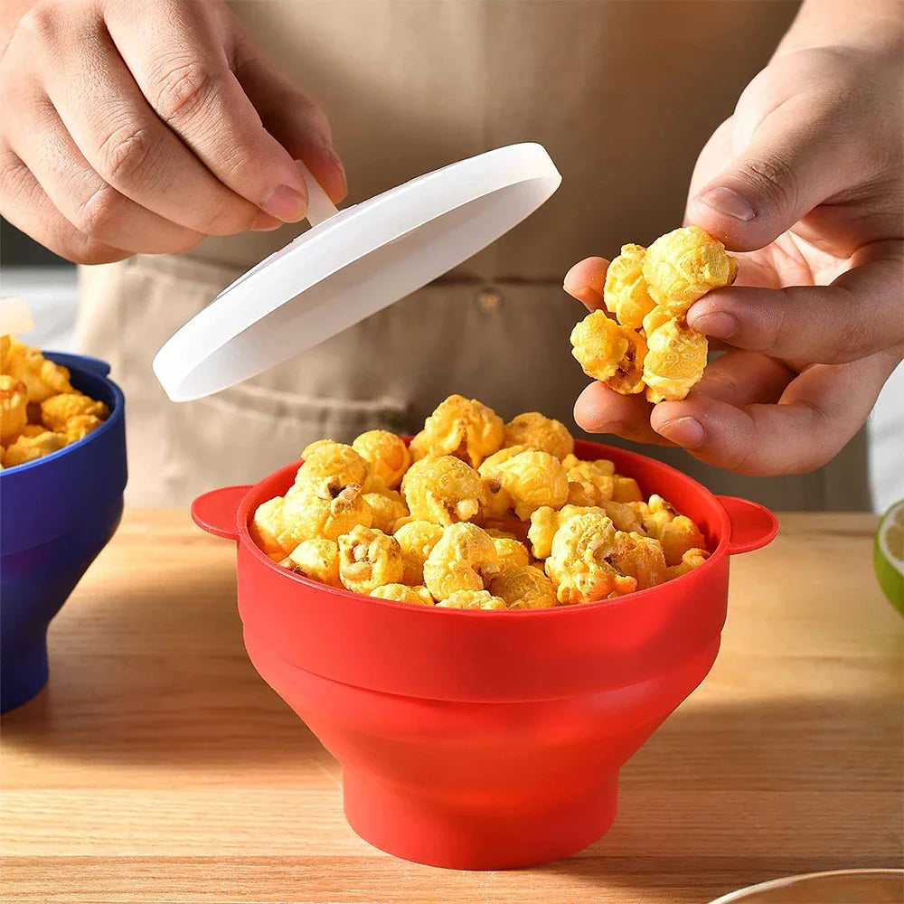 Hands are scooping yellow popcorn from a red silicone microwave bowl.