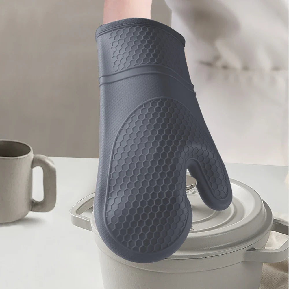 A close-up of a gray heat resistant silicone oven mitt with a textured pattern resting on a white pot.