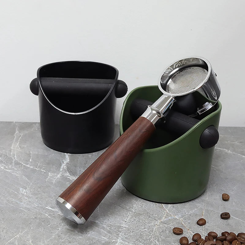 A stainless steel coffee grounds container with a wooden handle is shown next to a green storage cup on a gray surface.