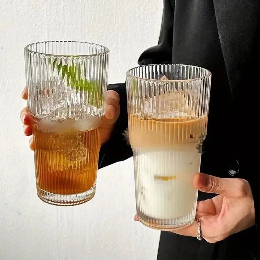 A person holds two glass drinking cups filled with iced beverages, one amber and one milky white.