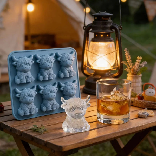 A set of blue silicone ice cube molds and a glass of amber liquid on a wooden table.