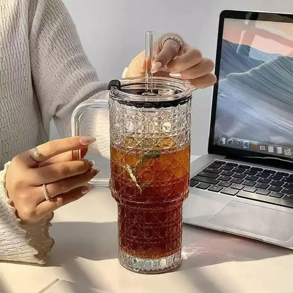 Ein Glas mit Eistee auf einem Schreibtisch neben einem Laptop, gehalten von einer Person.