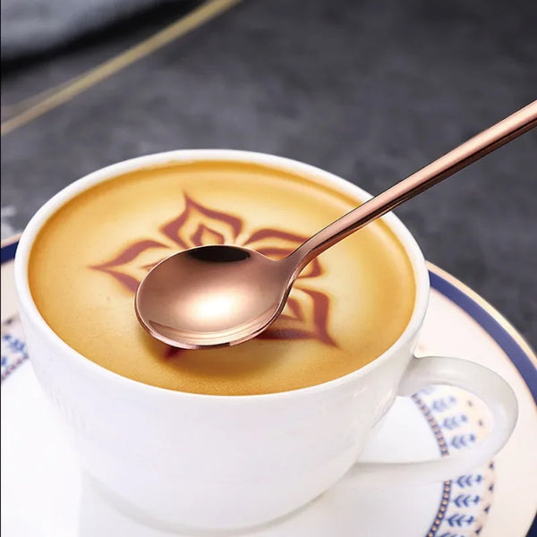 Eine kupferfarbene Löffel liegt in einer weißen Tasse Kaffee oder Tee vor einem dunklen Hintergrund.