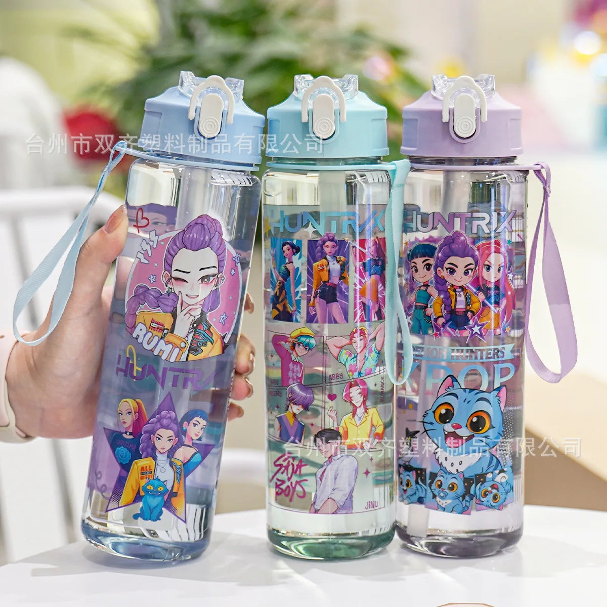 Three clear insulated water cups with colorful cartoon prints and light blue lids are displayed on a white surface.