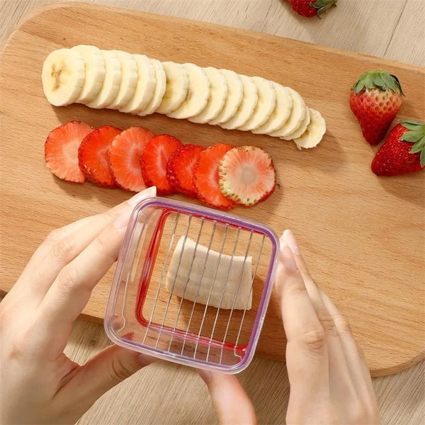 Hände benutzen einen klaren Plastikslicer, um Erdbeeren und Bananenscheiben auf einem Holzbrett zu schneiden.