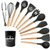 A set of black and wood silicone cooking utensils including a whisk, spatula, and various spoons and spatulas.
