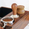 A precision espresso tamper set featuring a wooden handle and stainless steel base resting on a dark wooden surface.
