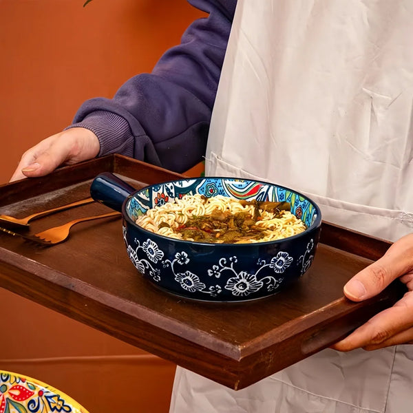 Eine Hand hält eine dunkelblaue Keramiksalatschüssel mit Reis und Gemüse auf einem Holzbrett.