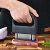 A hand holds a black stainless steel meat tenderizer with 48 needles over a cut of raw meat on a wooden board.