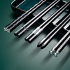 A set of five black chopsticks with gold accents are displayed on a dark green tray.