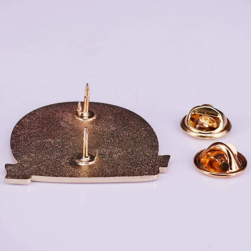 A set of gold-toned enamel pins and a brooch featuring a textured bronze finish.