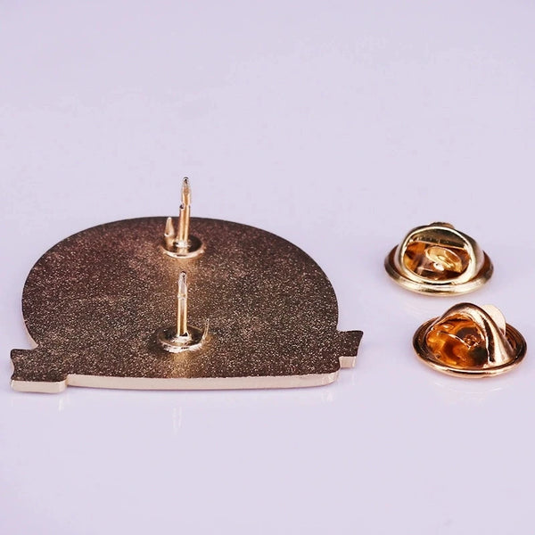 A set of gold-toned enamel pins and a brooch featuring a textured bronze finish.