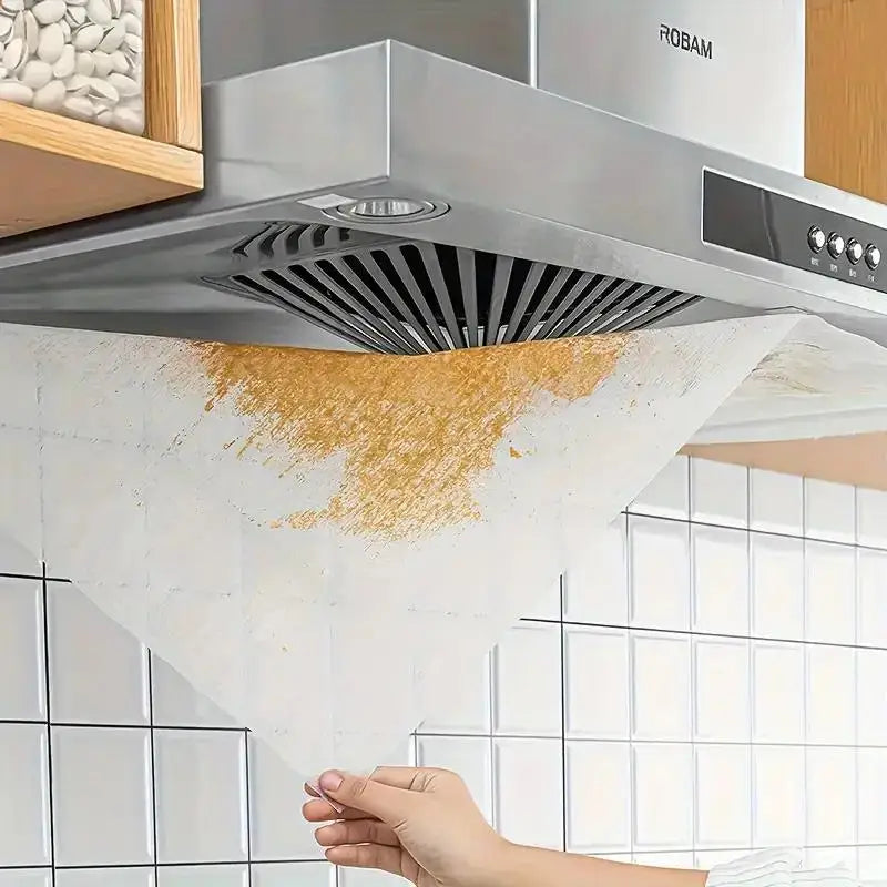 A hand is placing a paper filter into a stainless steel range hood for kitchen ventilation.