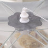 A white silicone food cover with a small stopper is placed on a gray mesh fabric for dining or picnic use.