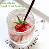 A glass mug filled with iced tea or beverage, garnished with mint and fruit, held by a dark straw.
