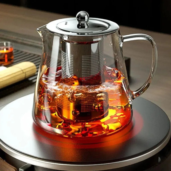 Elegier Borosilikatglas-Teegekoche mit Edelstahlfilter, gefüllt mit Bernsteintee auf einem Brenner.