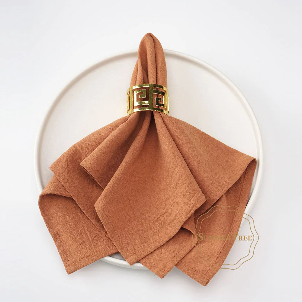A stack of ten rust-colored cotton table napkins tied with a gold-toned decorative band.