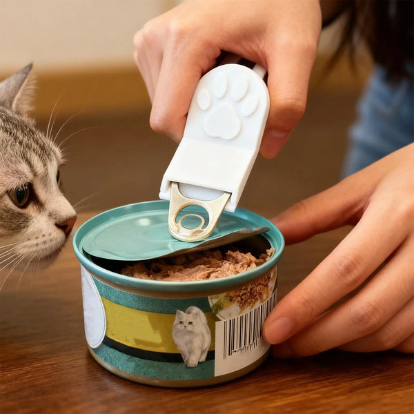 A hand is using a white pet food can opener with a paw grip to open a tin of dry pet food.