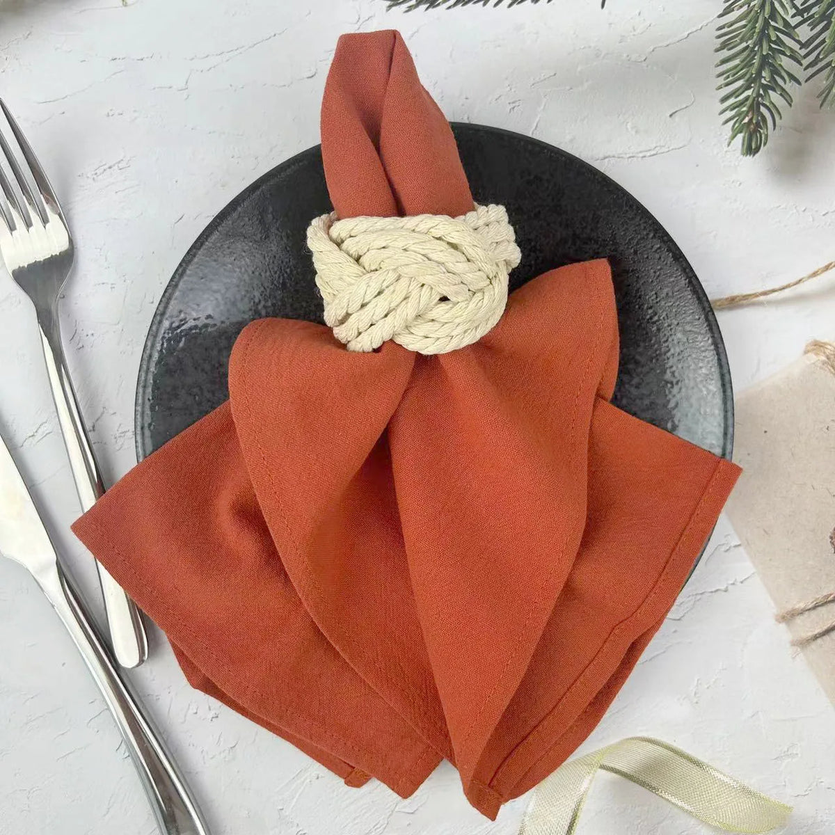 A set of six rust orange cloth napkins tied with natural twine displayed on a dark plate.