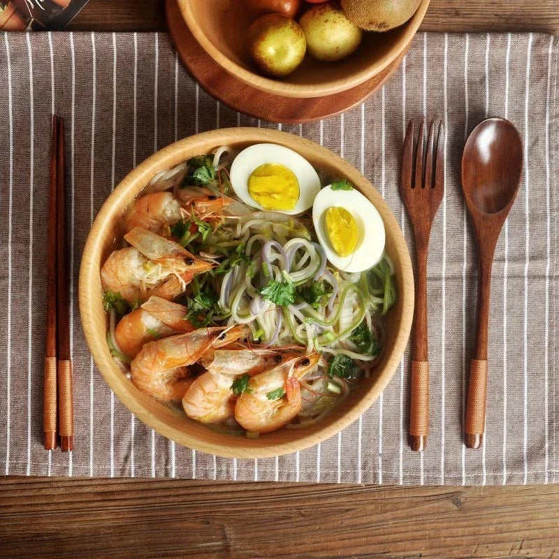 A bowl of cooked shrimp and vegetables served with a halved boiled egg, accompanied by a wooden cutlery set.