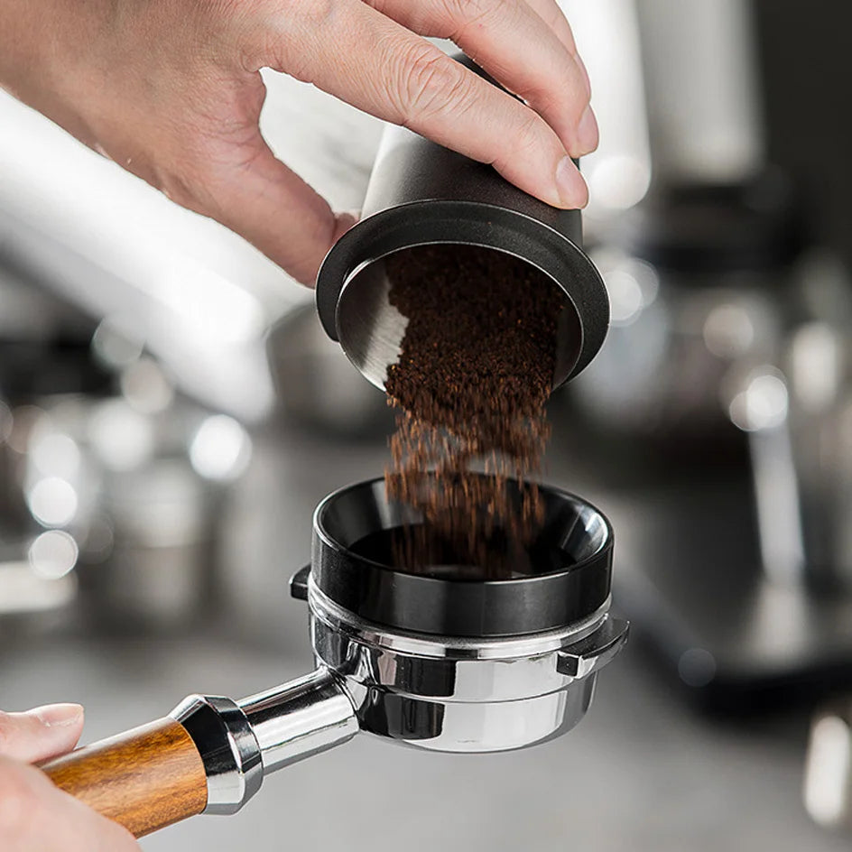 A hand pours dark coffee grounds into a stainless steel espresso coffee stirrer tool.