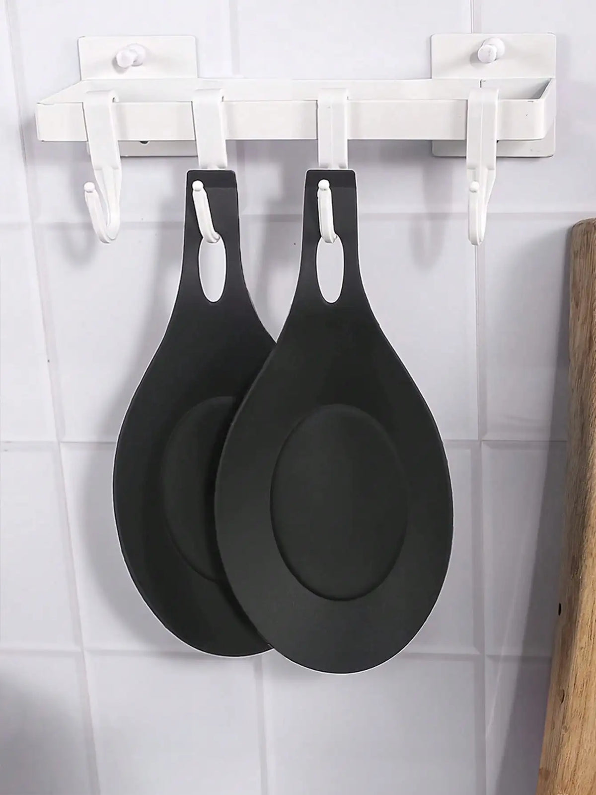 Two black silicone spoon rests or pot clips hanging from a white kitchen rack.