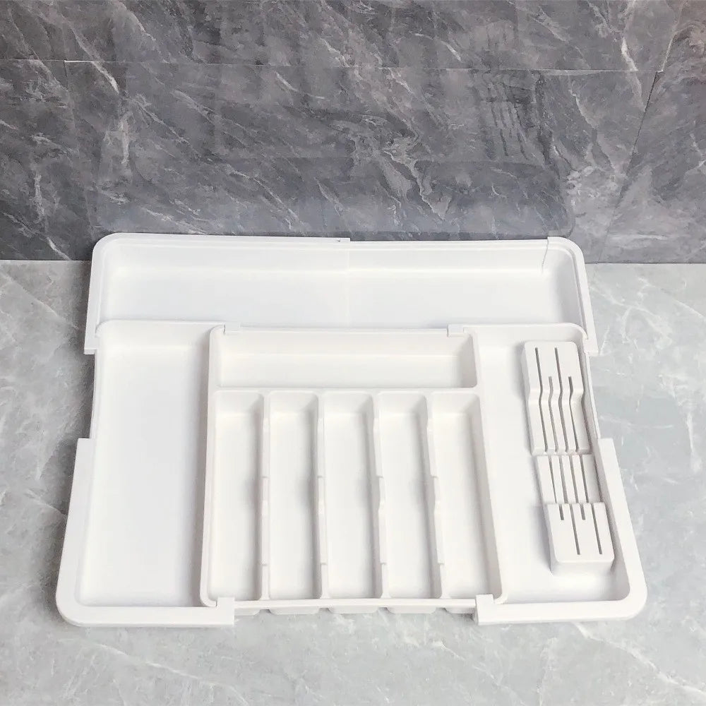A white retractable cutlery drawer organizer tray resting on a gray marble surface.