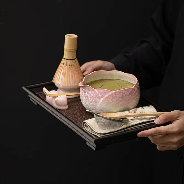 Ein Set rosa Keramik-Matcha-Verlader und eine Schale auf einem dunklen Tablett.