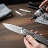 A hand applies precision knife pivot lubricant oil to a knife blade.