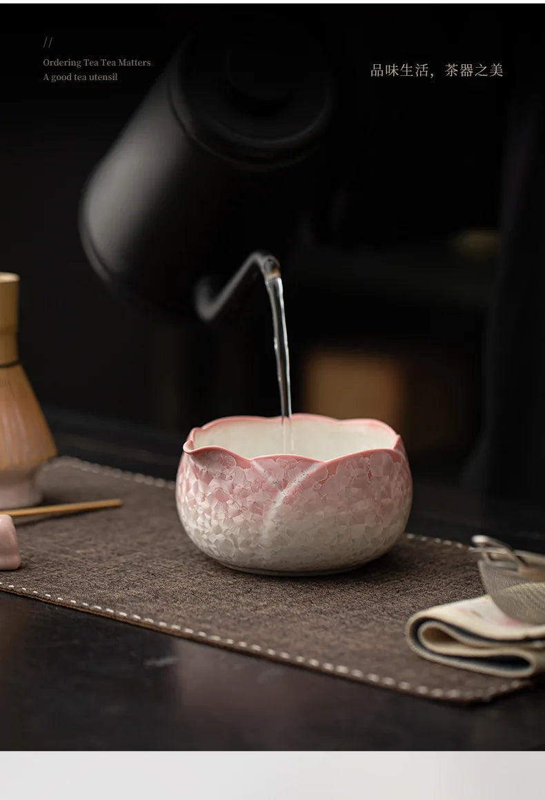 Un cuenco de cerámica rosa se está llenando de agua desde un utensilio para té en un entorno oscuro.