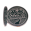 A round, antique-style enamel pin featuring the text I'm going on an adventure surrounded by a mountain and wavy lines.