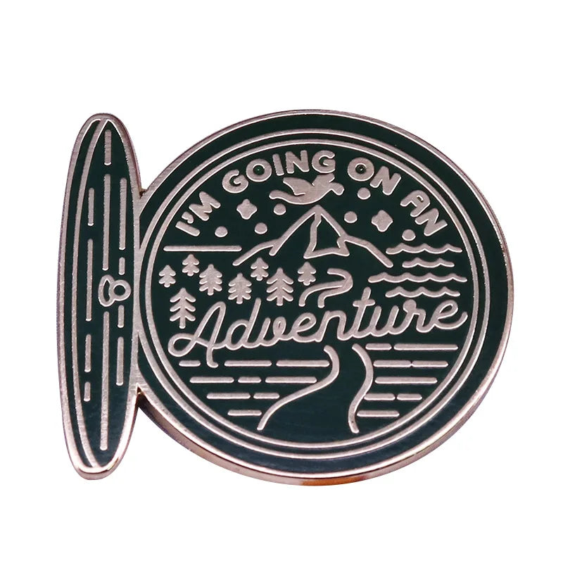 A round, antique-style enamel pin featuring the text I'm going on an adventure surrounded by a mountain and wavy lines.