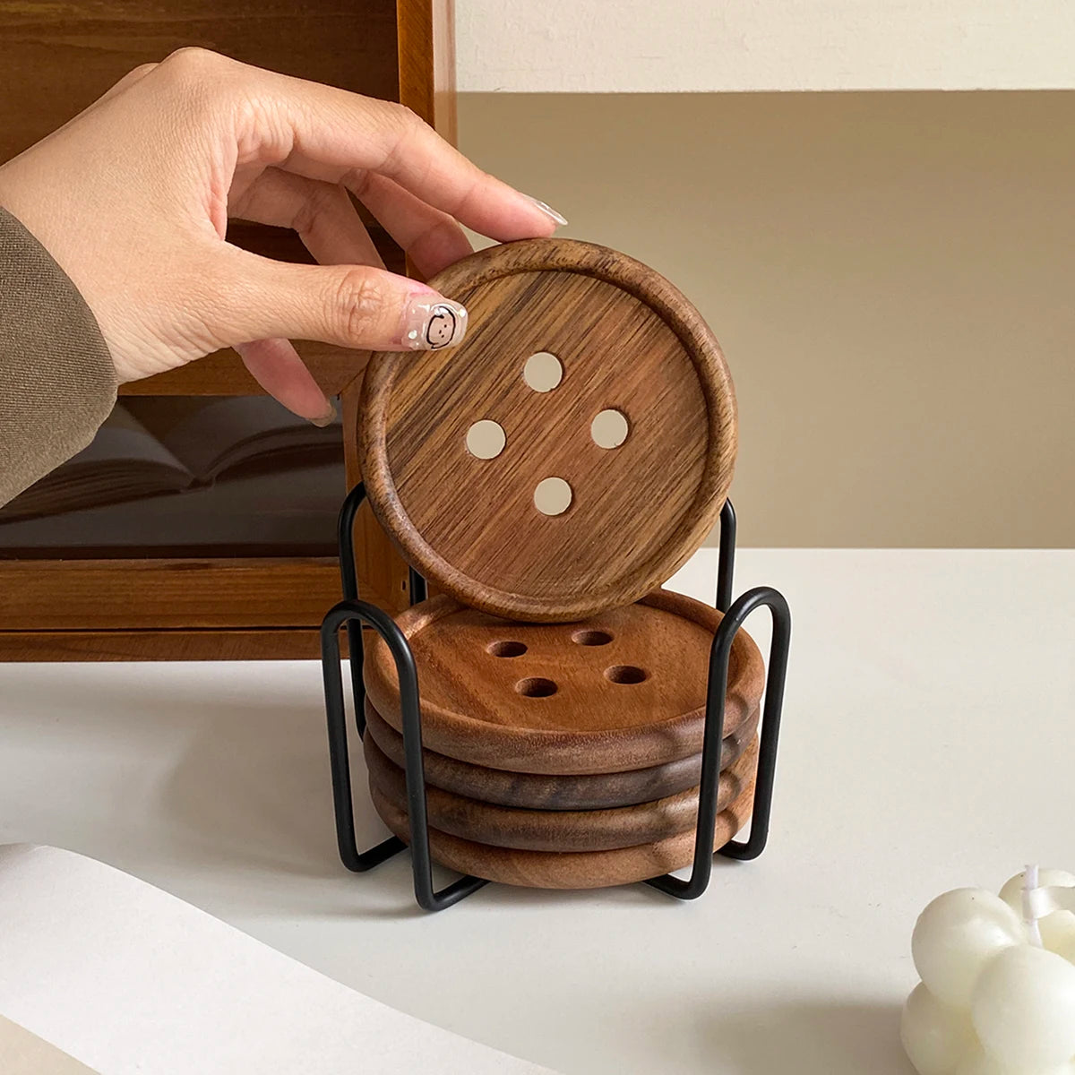 A hand is holding a round wooden coaster and a stack of coasters with an iron rack on a white surface.