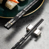 A pair of reusable multi-color chopsticks with silver accents resting on a gray surface next to sushi.